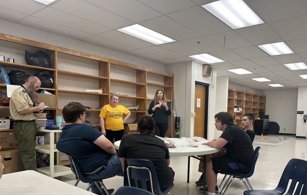 Boy Scout participants seated around a circular table as they meet with their Scout Leader.