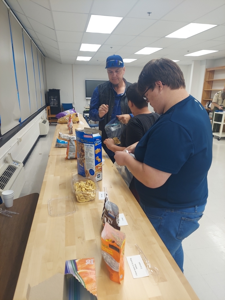 Two students and a male Residential Care Specialist (RCS) making trail mix snacks.