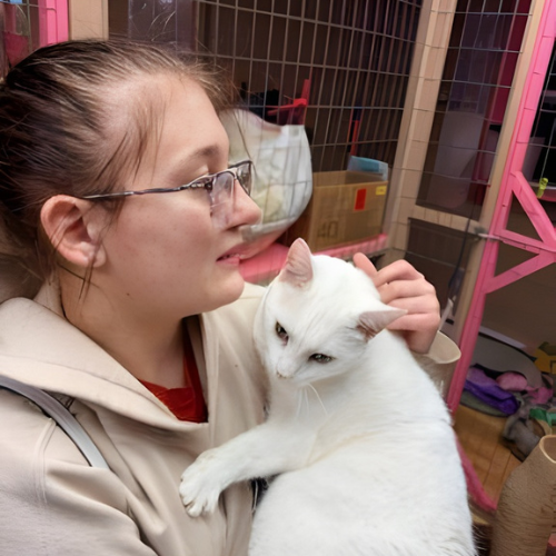A female wearing glasses holds a white cat in her arms.