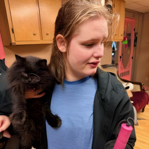 A female with dark hair holds up a black cat.