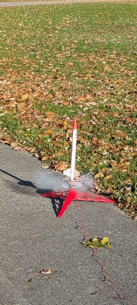 A white rocket gets ready to launch off of a red-colored launchpad as a stream of smoke comes out of the bottom.