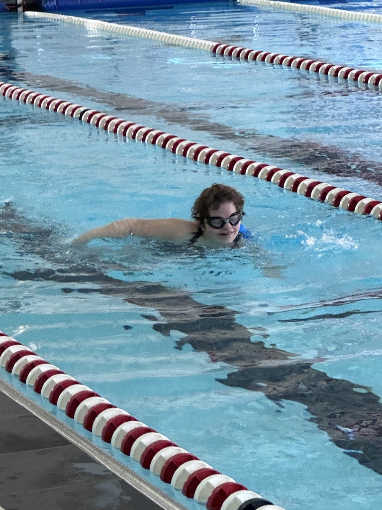 A female student-athlete wearing goggles smiles as she swims in the pool.