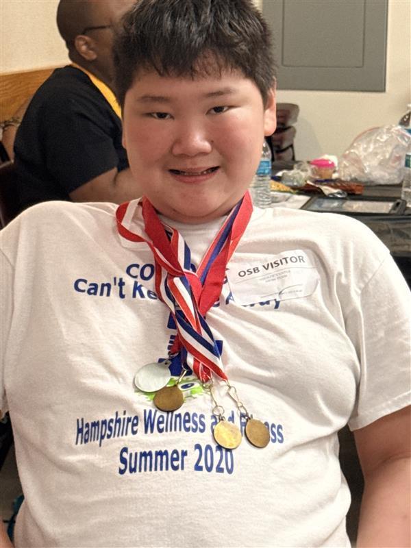 A male student wearing a white shirt as he poses with his medals around his neck.