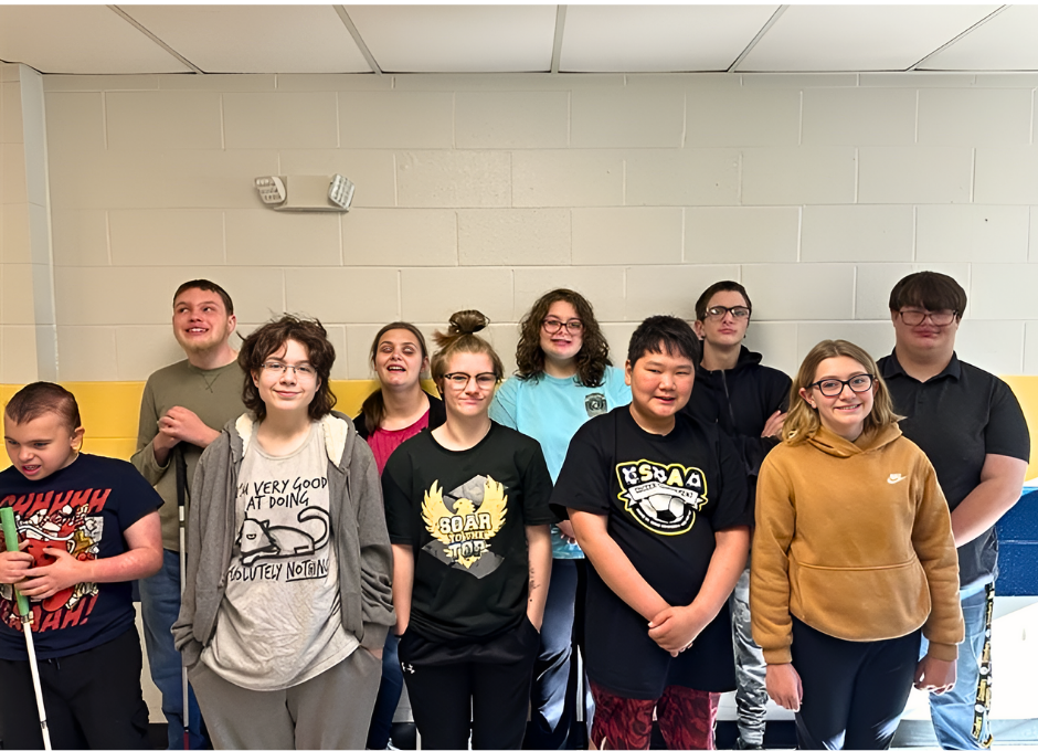 Students stand side-by-side in two separate rows in front of a white wall with blue and yellow stripes.