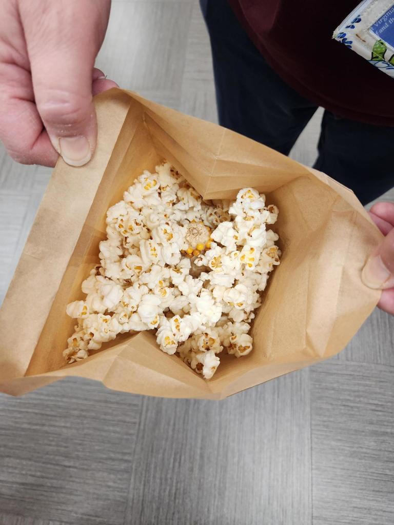 A brown paper bag full of popped popcorn.