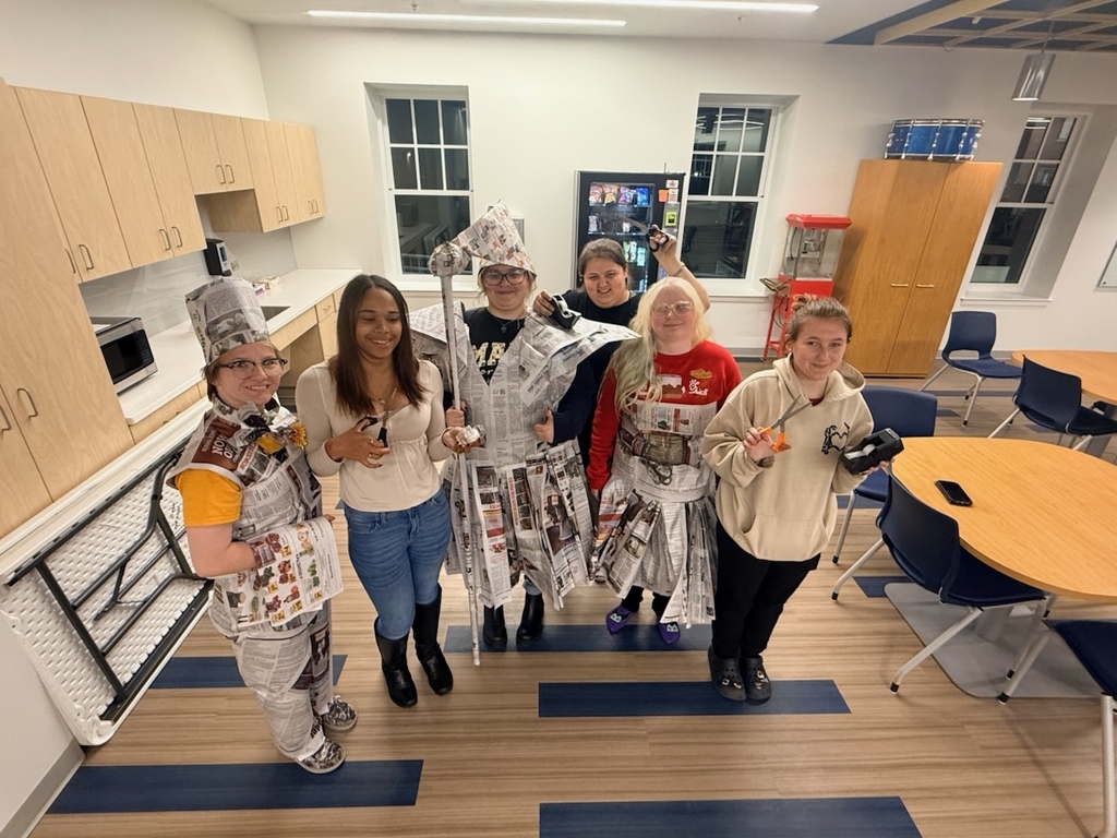 A group photo of attendees standing side by side. Some of them are wearing costumes made out of newspaper.
