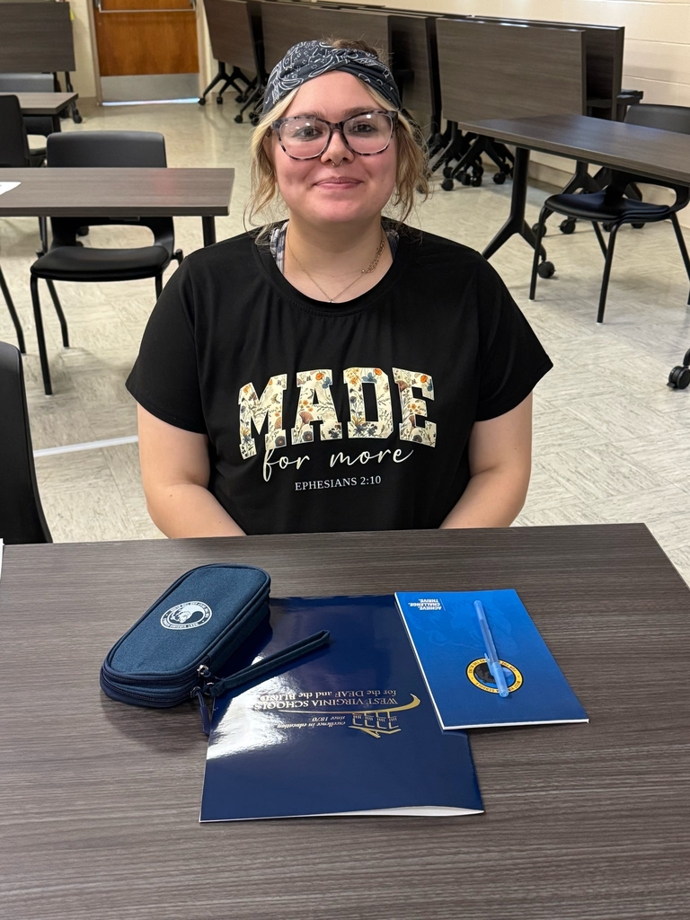 A female attendee wearing glasses and a blue bandana smiles for the camera as she is seated at a table with resources sitting in front of her.