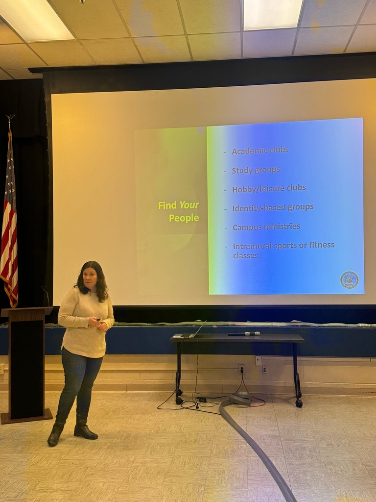 A female presents a presentation using a large screen behind her.