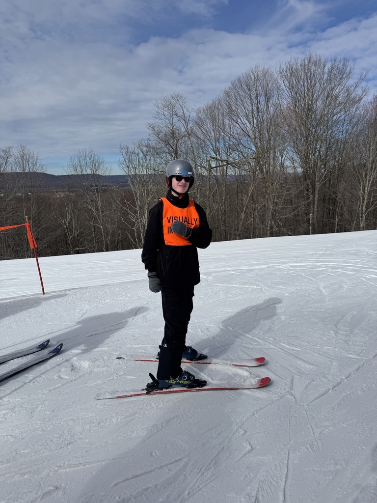 A male skier in winter gear looks towards the camera as he is surrounded by white-colored snow.