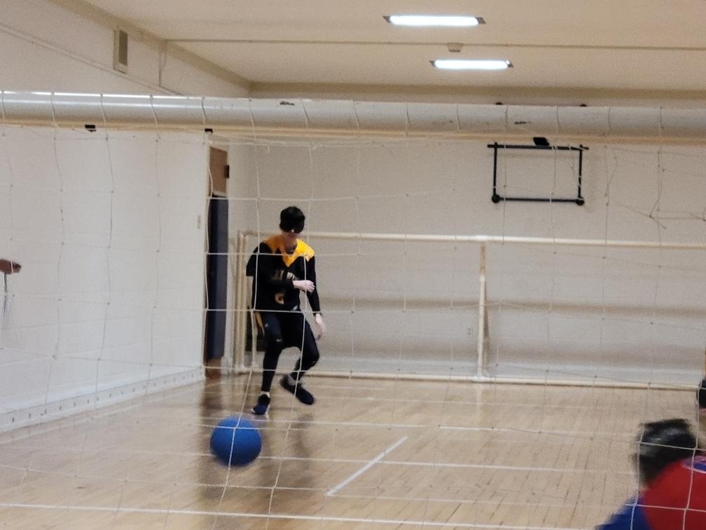A male goalball player rolls a blue-colored goalball.