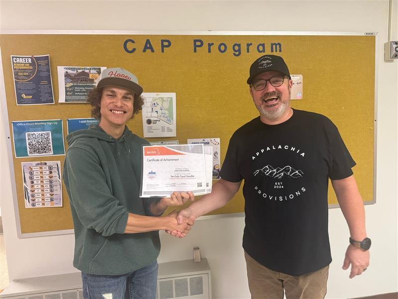 A male student proudly holds up a certificate as he shacks hands with ProStart Culinary instructor Chef Brian Olden.