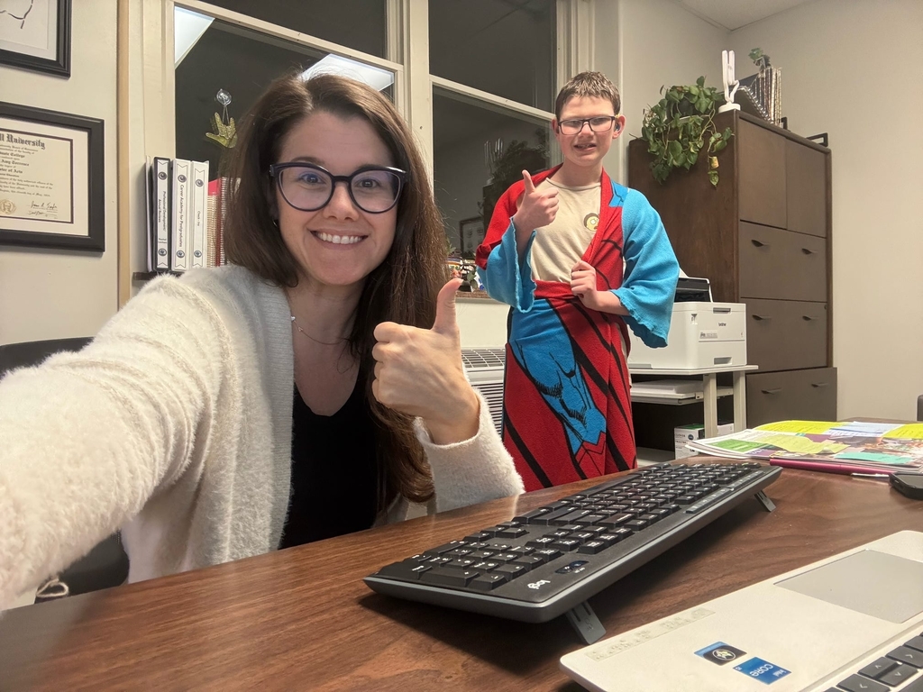 Ms. Rachel Lanham, a female with dark hair and glasses takes a selfie with a male student wearing glasses. They both are giving a "thumbs up."