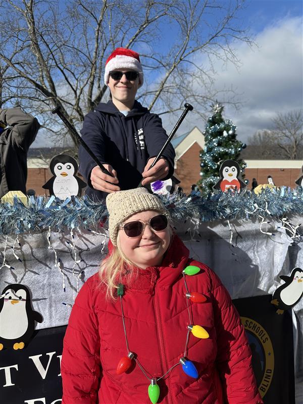 A male student stands on the parade float and pretends to "drum" on a female student's head with his drumsticks.