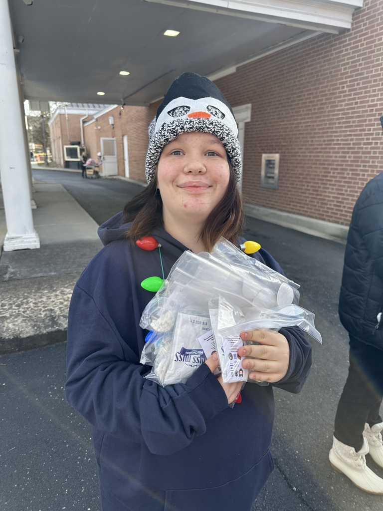 A female student wearing a navy sweatshirt and a light-up necklace holds packs of hot chocolate in her hands.