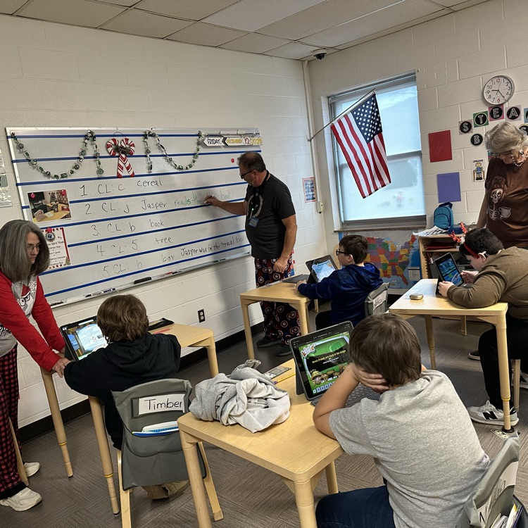 Elementary students are seated at their desks while staff members are dressed in pajamas. 
