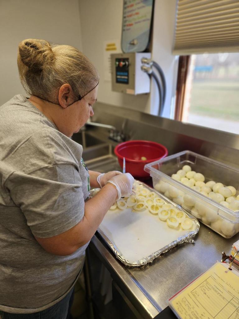 A female kitchen staff member wearing a gray-colored shirt has her back towards the camera as she works on deviled eggs.