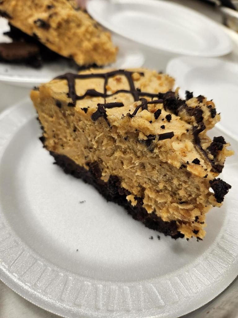 An up-close photo of a piece of chocolate cake with a chocolate drizzle on a white-colored paper plate.