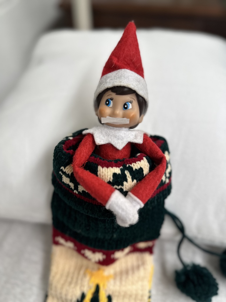 A toy elf dressed in red and white attire is tucked into a festive print sock.