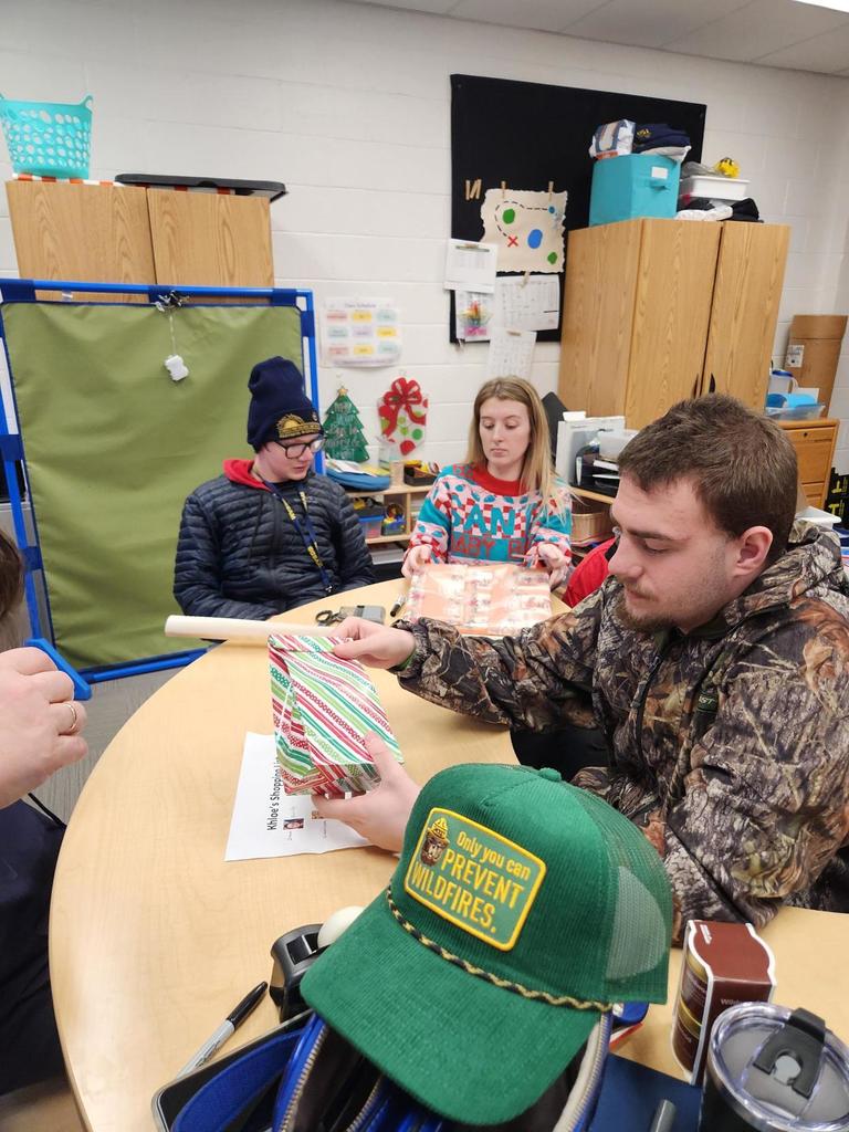 CAP students are seated at a table as they work together to assist elementary students with wrapping their gifts.