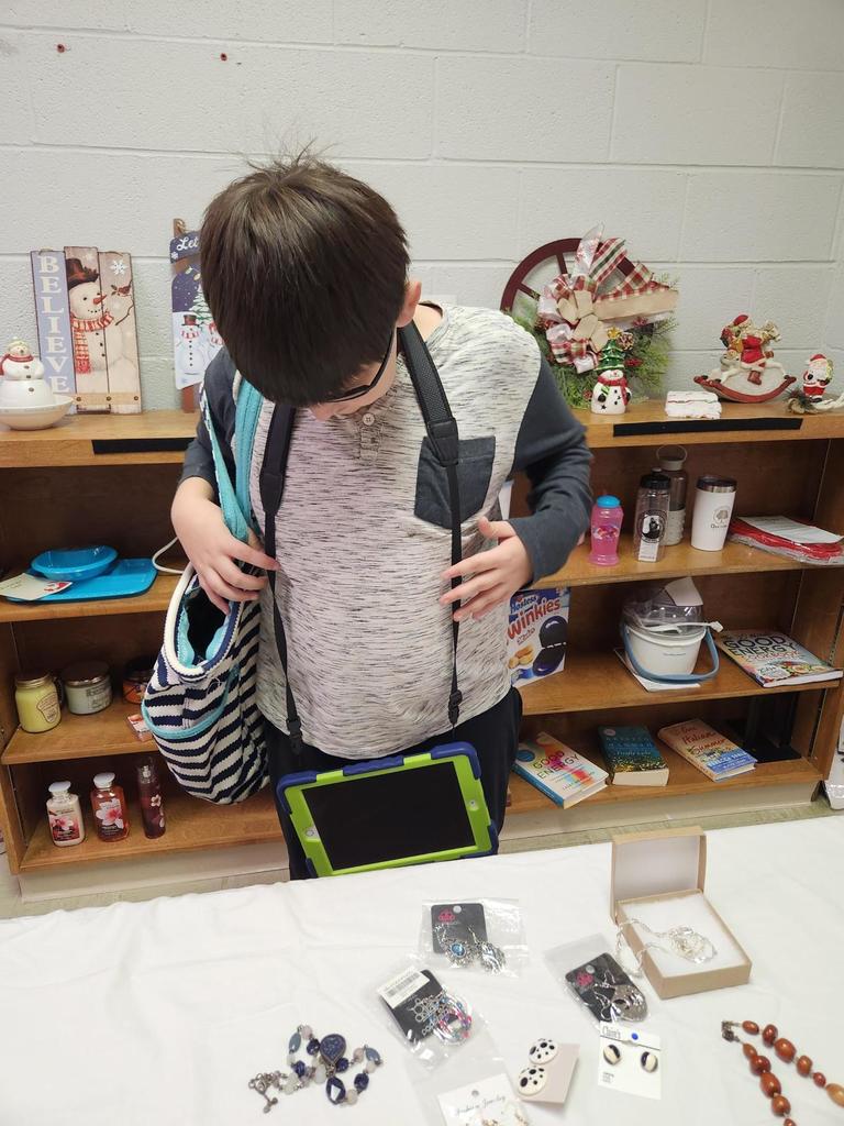 A male student wearing a gray-colored shirt and dark brown hair looks down at the gifts that are available for purchase on a table.