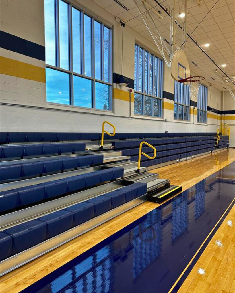 An overview of the updated, blue-colored bleachers featuring yellow accents. Above the bleachers are a wall of windows. 