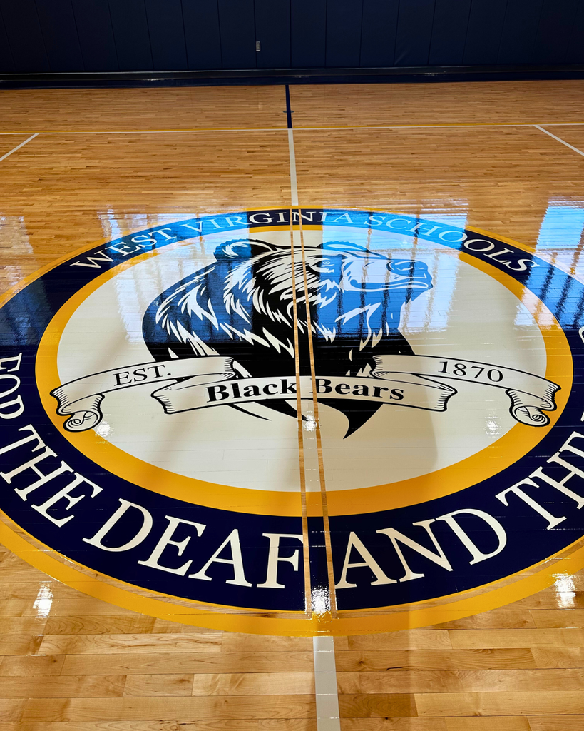 WVSDB Black Bear logo featuring an outline of a black bear surrounded by blue and gold circles painted onto the gymnasium floor. 