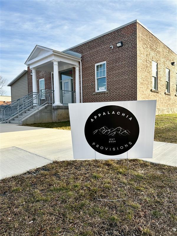 The exterior of the Blue and Gold building with a black and white Appalachia Provisions yard sign in the front of the building.