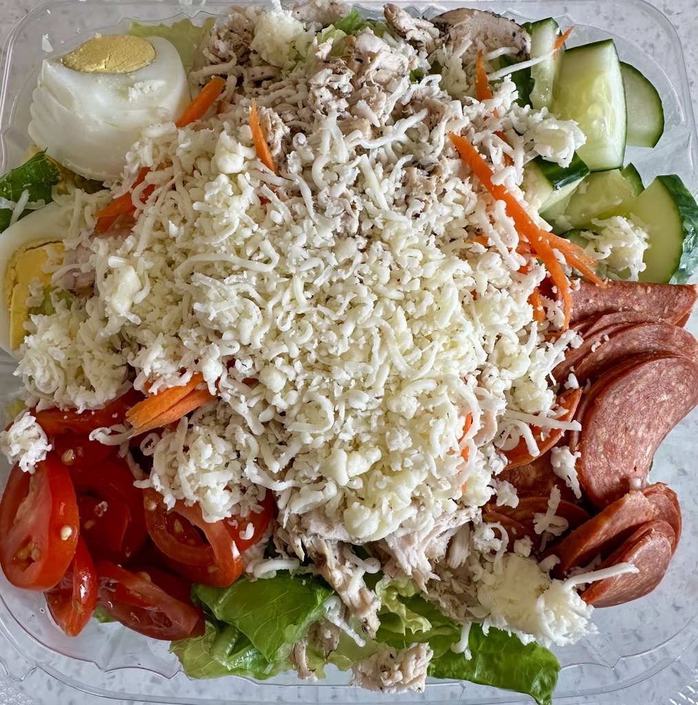An Italian salad featuring a bed of green lettuce with pepperoni, cucumber, tomatoes, boiled eggs, and cheese sprinkled on top.