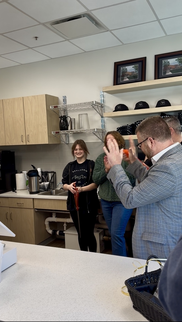 Two females officially cut the red-colored ribbon, while spectators cheer. The female holding the scissors smiles proudly.