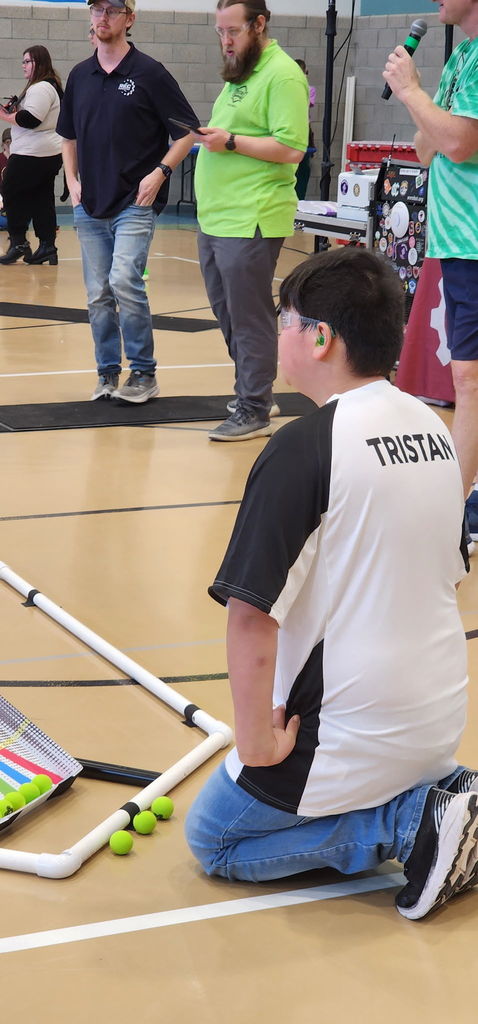 A male student is kneeling down and wearing safety glasses as he looks towards the drone course.
