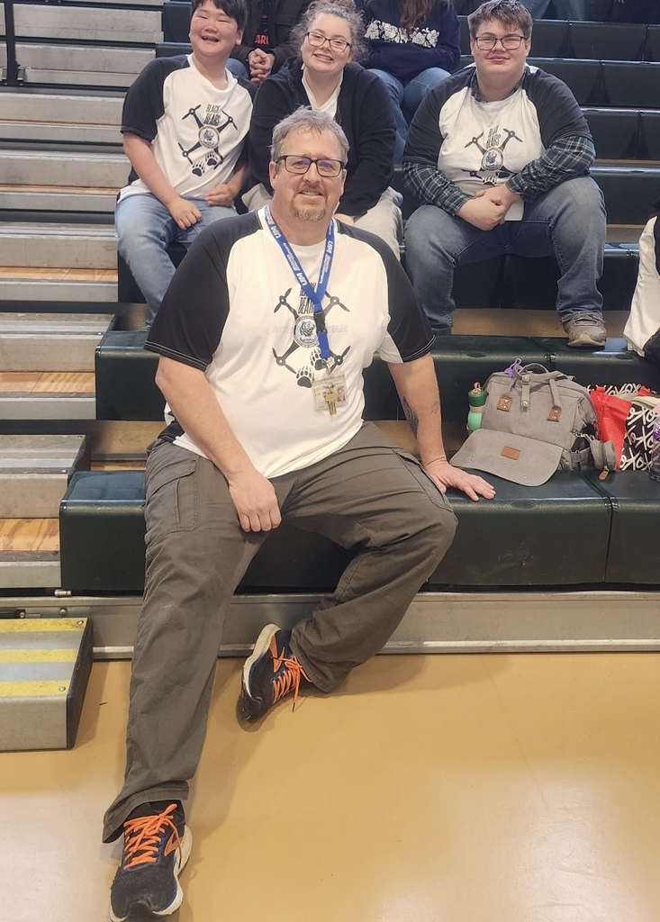 Students and their male coach are seated on bleachers and smile for the camera. 