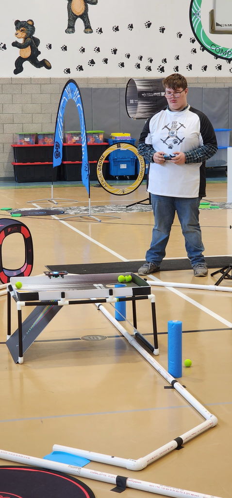 A male student stands and holds a remote controller as he concentrates on flying his drone through the course. 