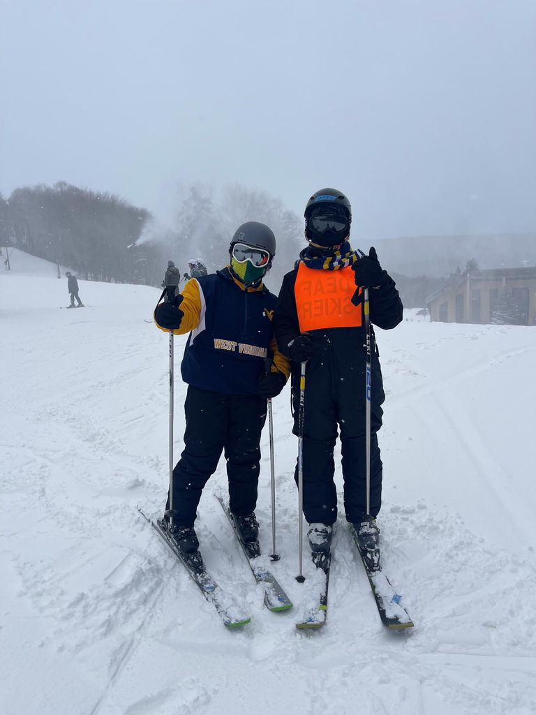 Two skiers stand side-by-side in their ski gear surrounded by white snow. 