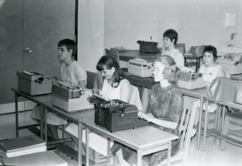 A group of students seated at their desks with a Braille writer in front of each student.