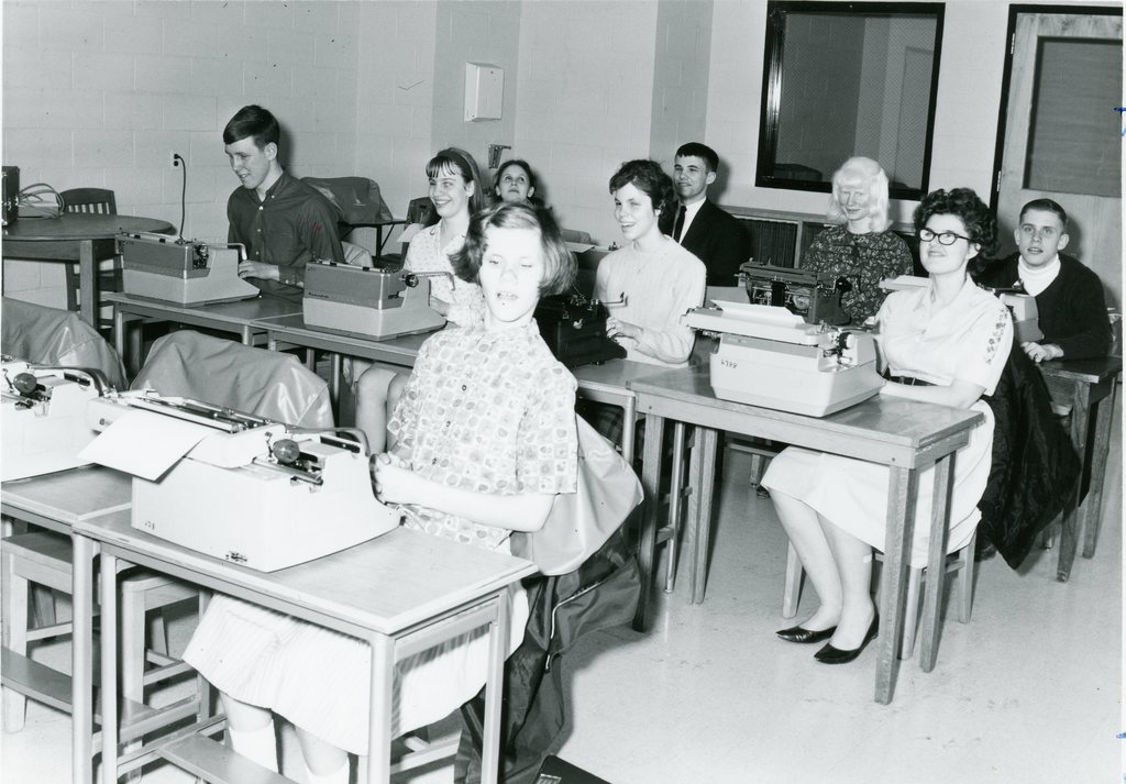 A group of students seated at their desks with a Braille writer in front of each student.