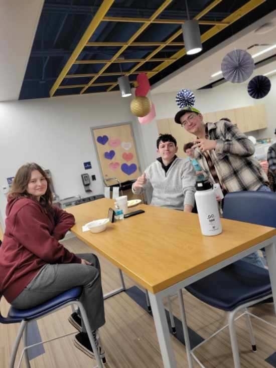 Residential students are seated and gathered around a high-top table in the student union. 