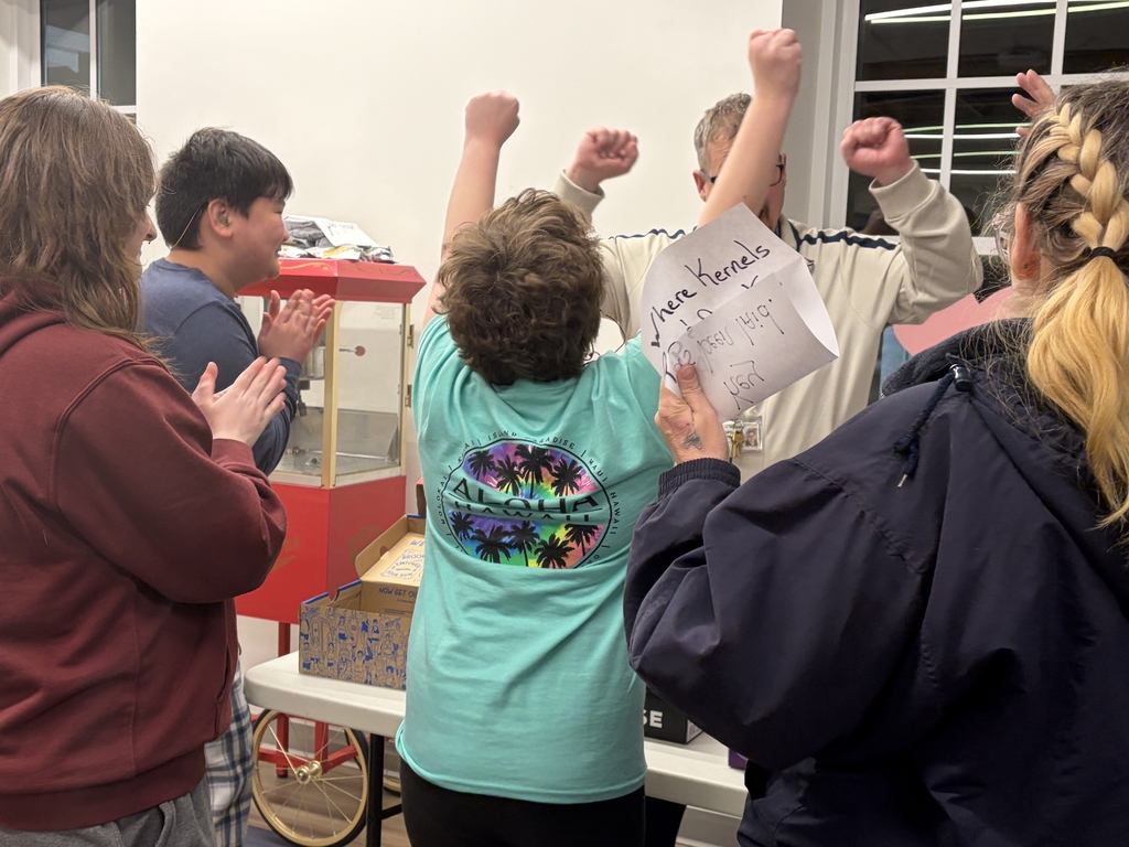 Students and Residential Care Specialists are gathered around a table cheering with their arms in the air for celebration. 