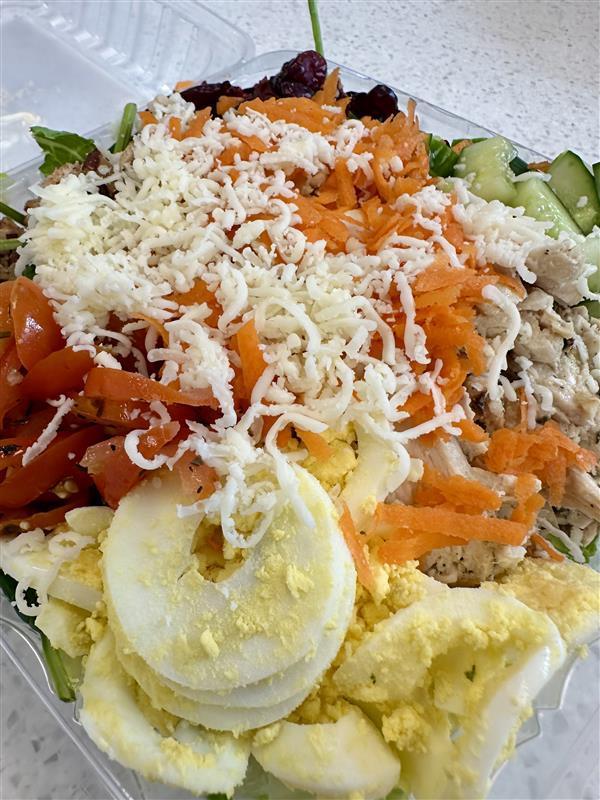 Pecan Cranberry Chicken Salad featuring cheese, tomatoes, carrots, hard-boiled eggs, on a bed of green lettuce.