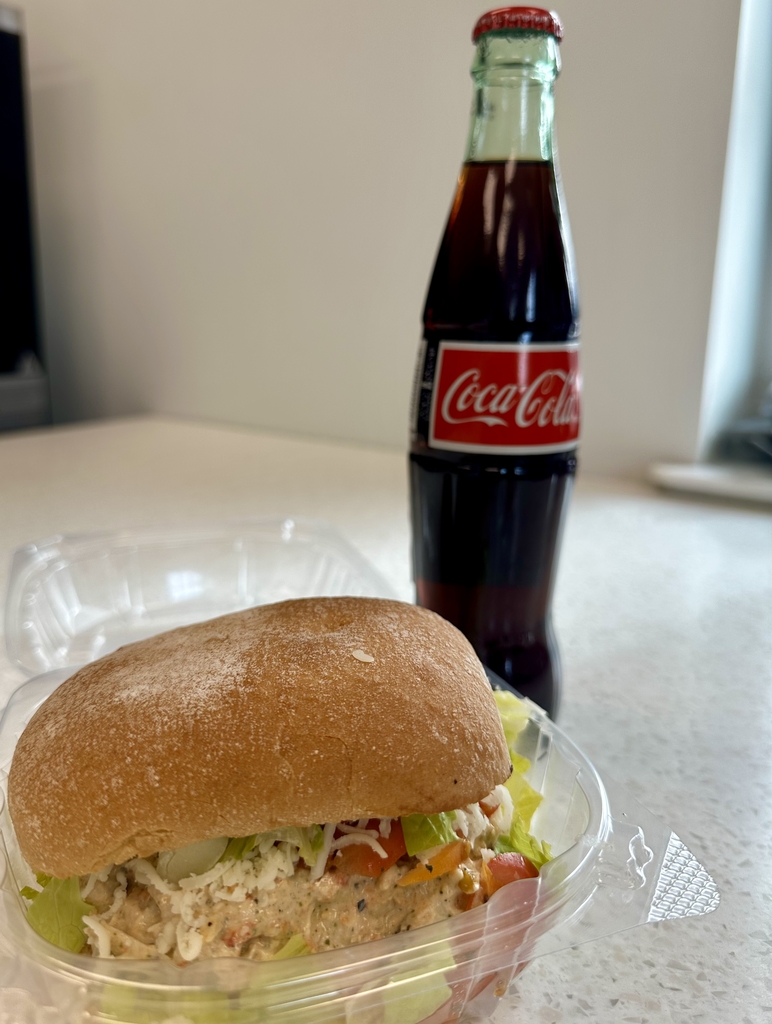 Pesto Caprese Chicken on Ciabatta sandwich with a coke in a glass bottle to the right of the sandwich. 
