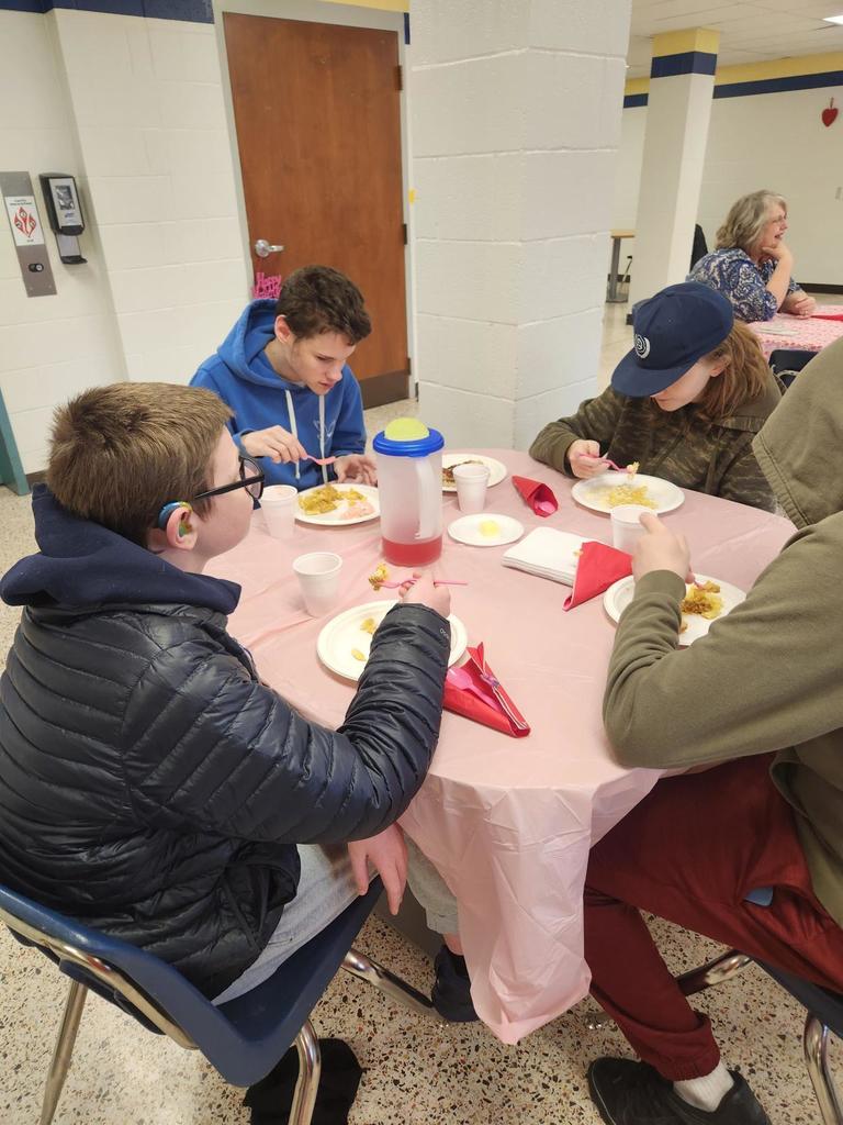 CAP students seated at a circular table with a pale pink tablecloth on top enjoy their pasta meal.