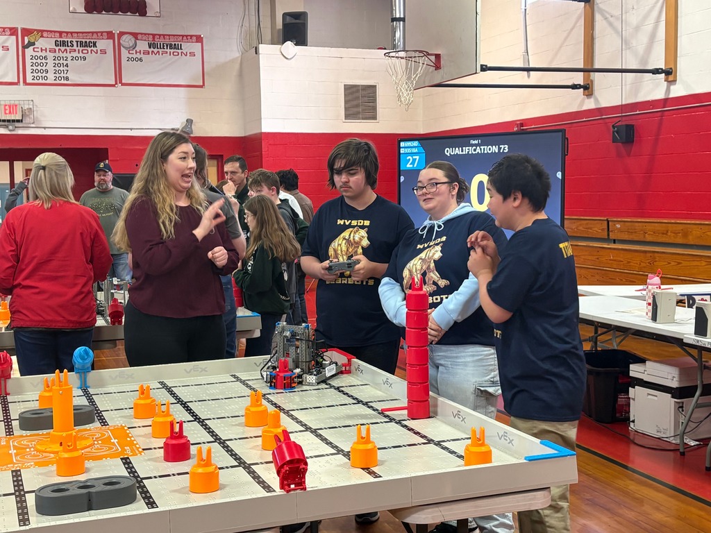 WVSDB Bearbots Robotics team gathered around a robotics arena. A male team member in the middle is holding a remote controller to control the robot. 