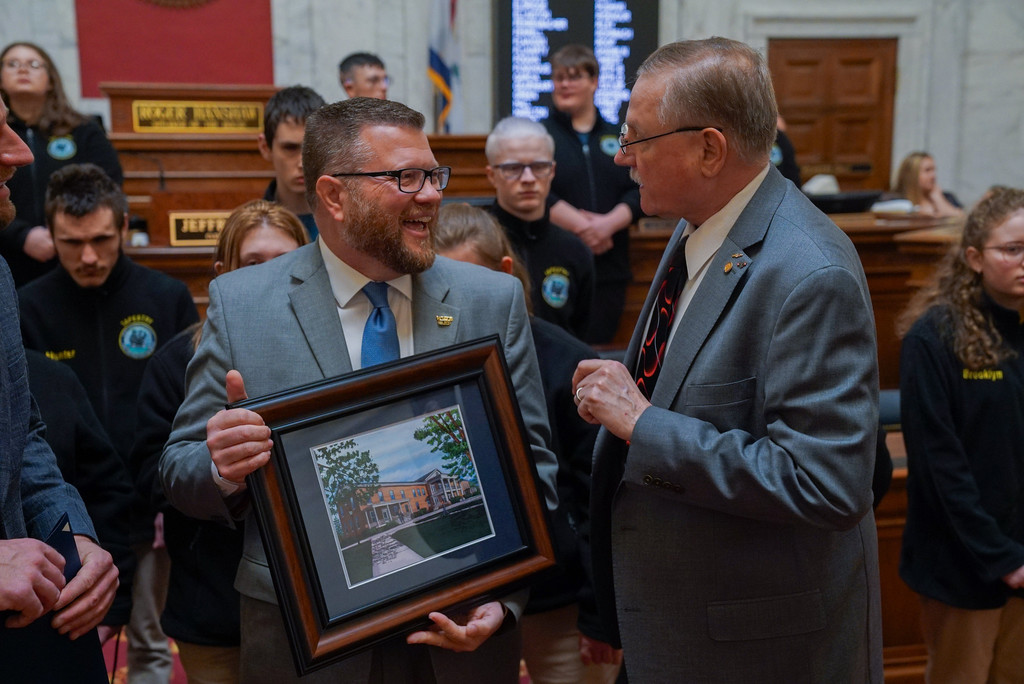 Superintendent Clayton Burch smiles proudly at Delegate Hillenbrand. Superintendent Burch is holding up a print of the former WVSDB Administration Building. 