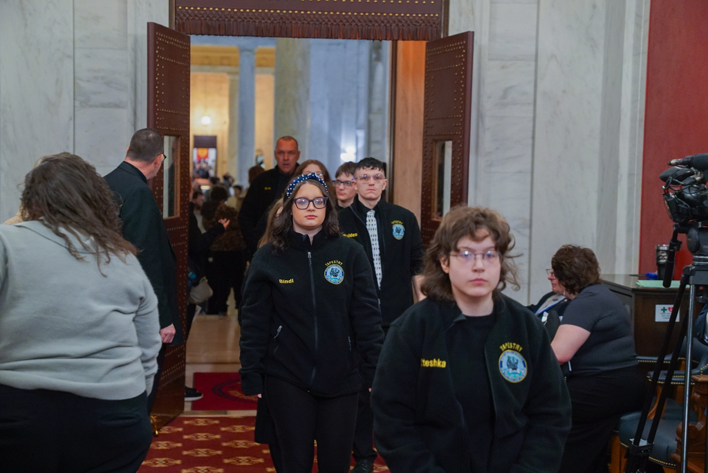 A group of WVSDB students walking into the Legislature room wearing matching black fleece jackets.
