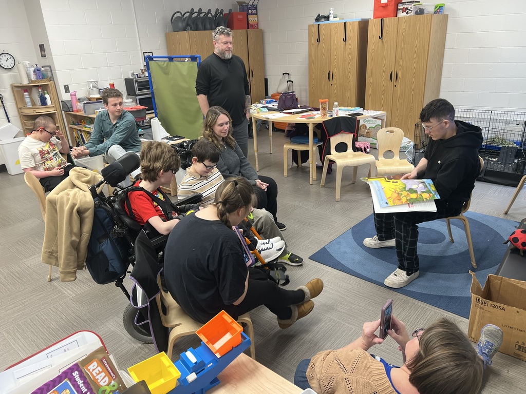 A male high school student is seated with a book in his lap as he turns the page of the book. 