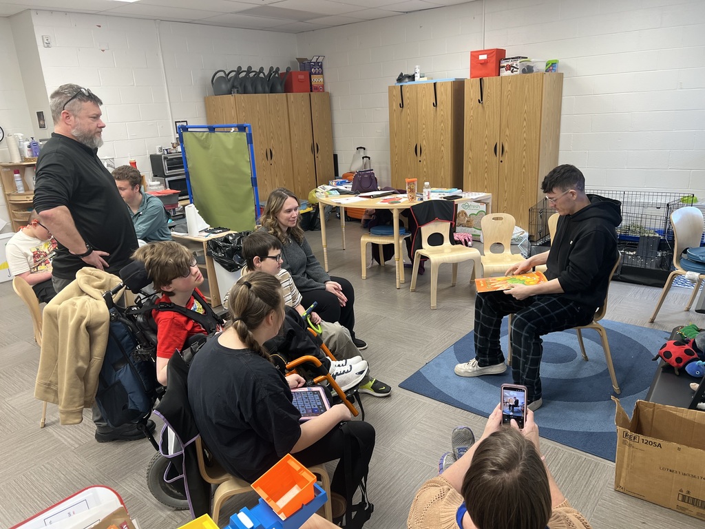 A male high school student is seated with a book in his lap as he turns the page of the book. 