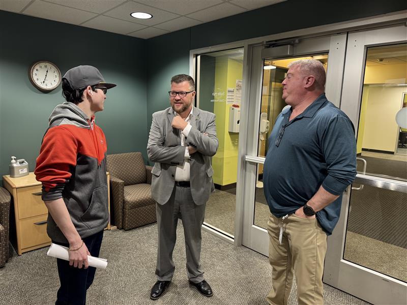 Three male individuals stand together talking and mingling with one another.