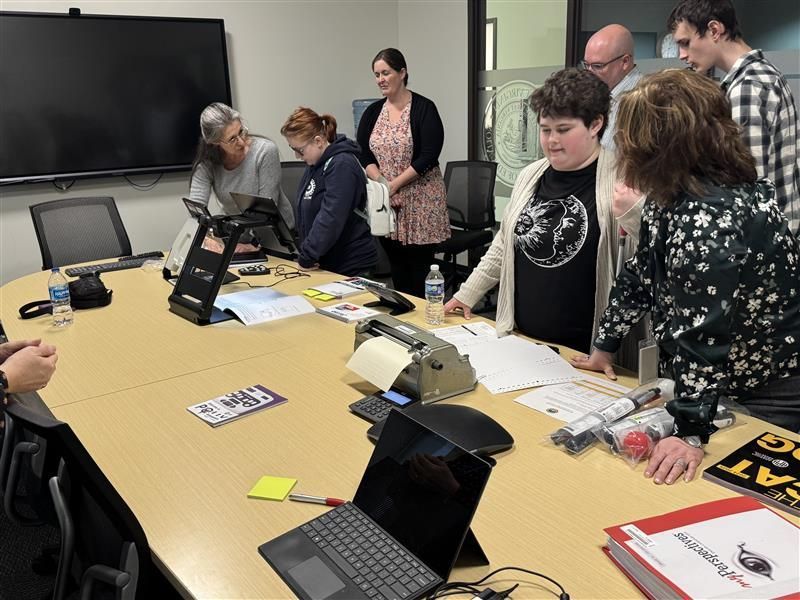 Individuals are gathered around a large conference table as they are educated on technology from the Instructional Resource Center (IRC).