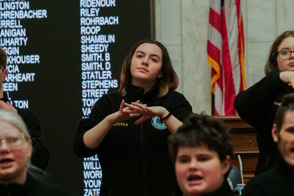 A female WVSDB student wearing a black, fleece jacket uses American Sign Language (ASL) to interpret the performance during the legislative event. 