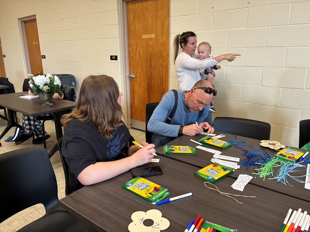 Deaf Social participants are seated at a table doing crafts using markers and colored pencils.