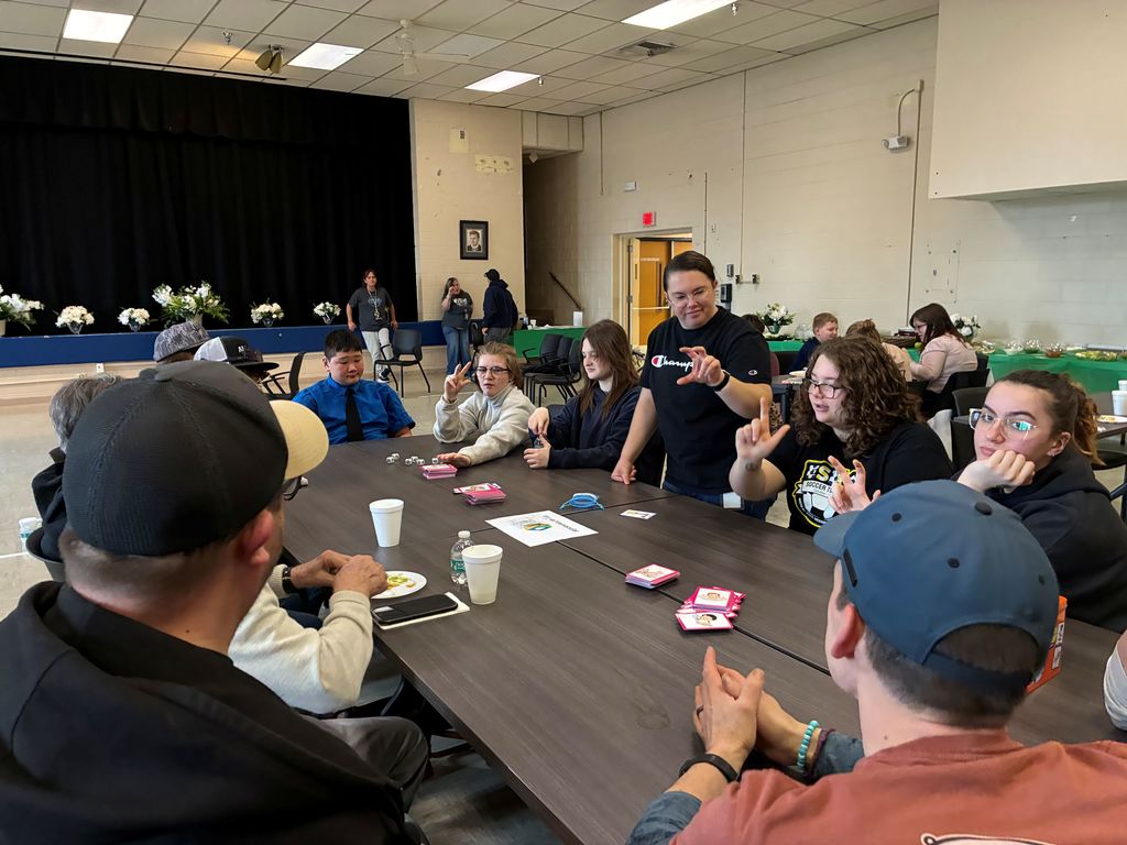 Participants are seated at a table using American Sign Language (ASL) and playing card games.